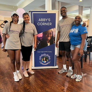 Four attendees pose with the Abby's Corner banner