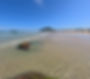 Beira-mar da praia do Santinho, com água transparente, ilhas e costão ao fundo.