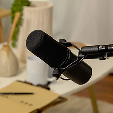 Podcast microphone in the foreground with a coffee table decorated with mugs and pots in the background