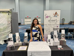 Romance author Tori Alvarez standing behind a table decorated with her books at SpicyReads book convention. 