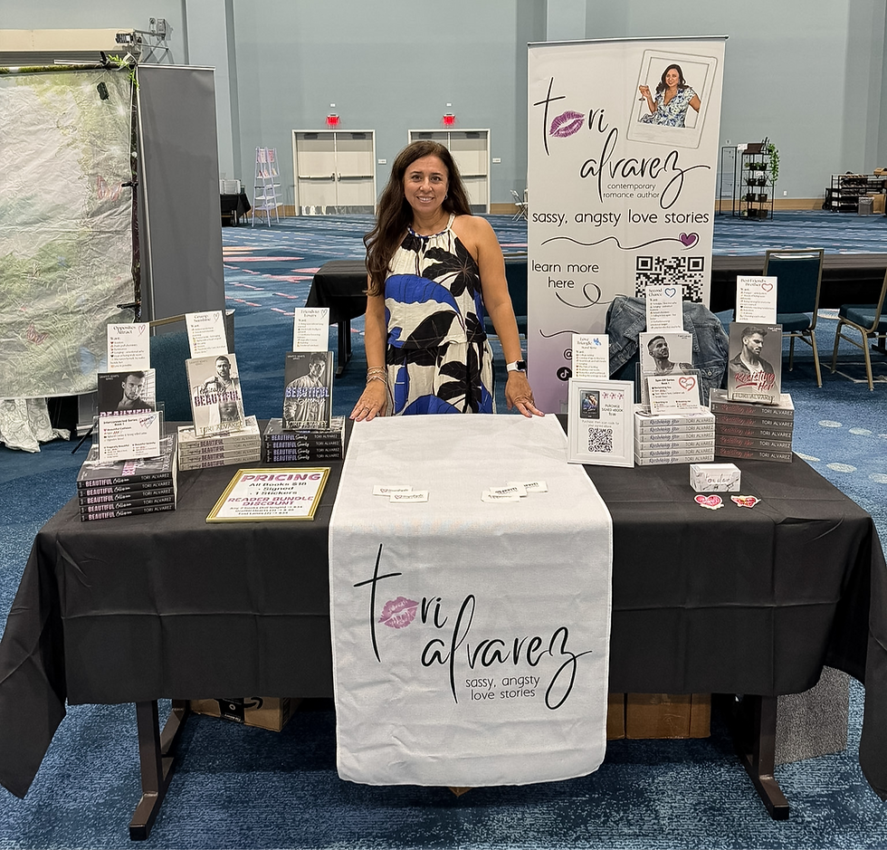 Romance author Tori Alvarez standing behind a table decorated with her books at SpicyReads book convention.