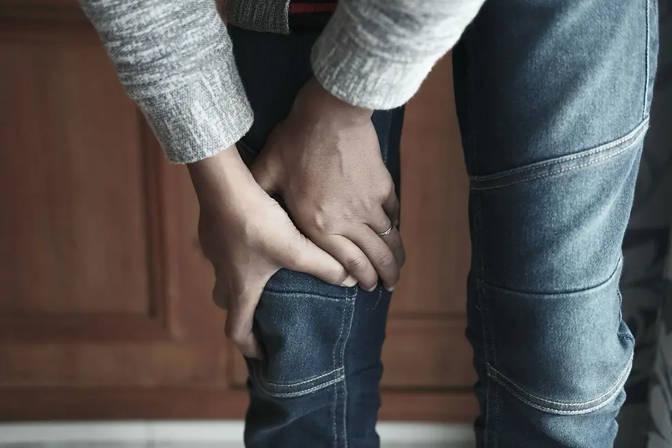 Gros plan sur deux mains tenant fermement un genou à travers un jean, personne debout.