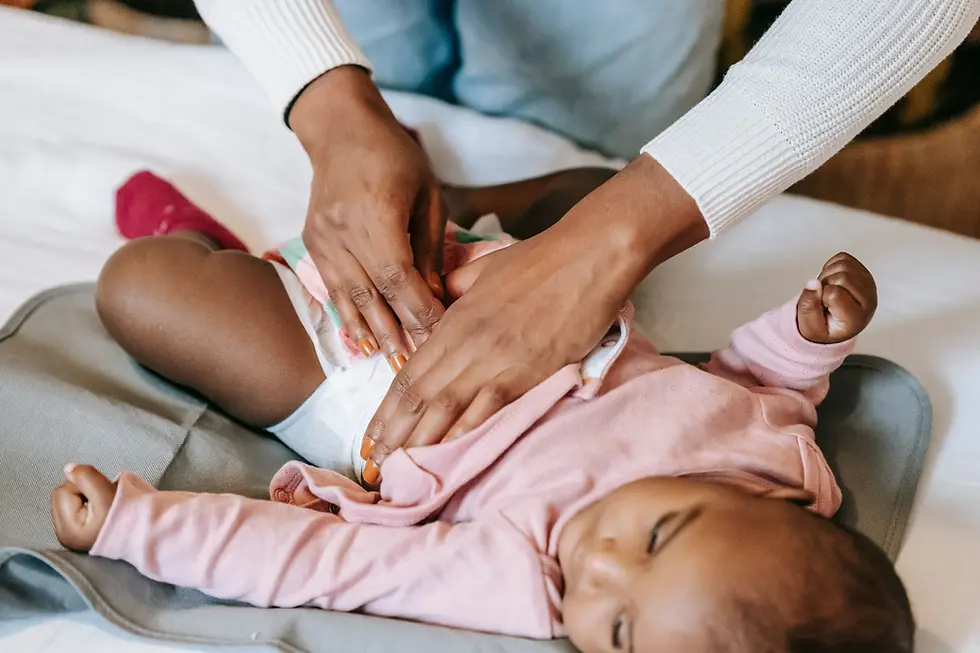 Mains d'un parent changeant la couche d'un bébé vêtu d'un pyjama rose, allongé sur un matelas à langer gris.
