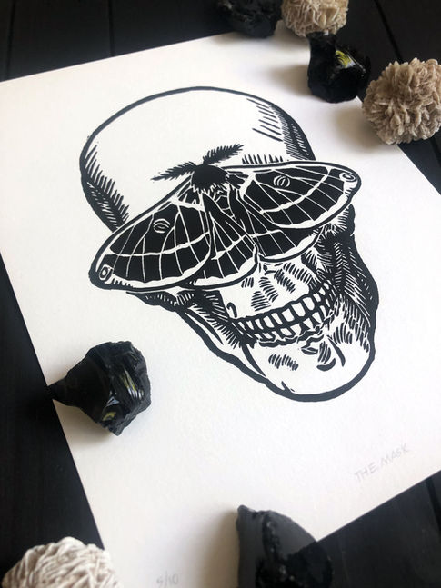 Linocut print of a human skull with a moth over its eyes, titled "The Mask"