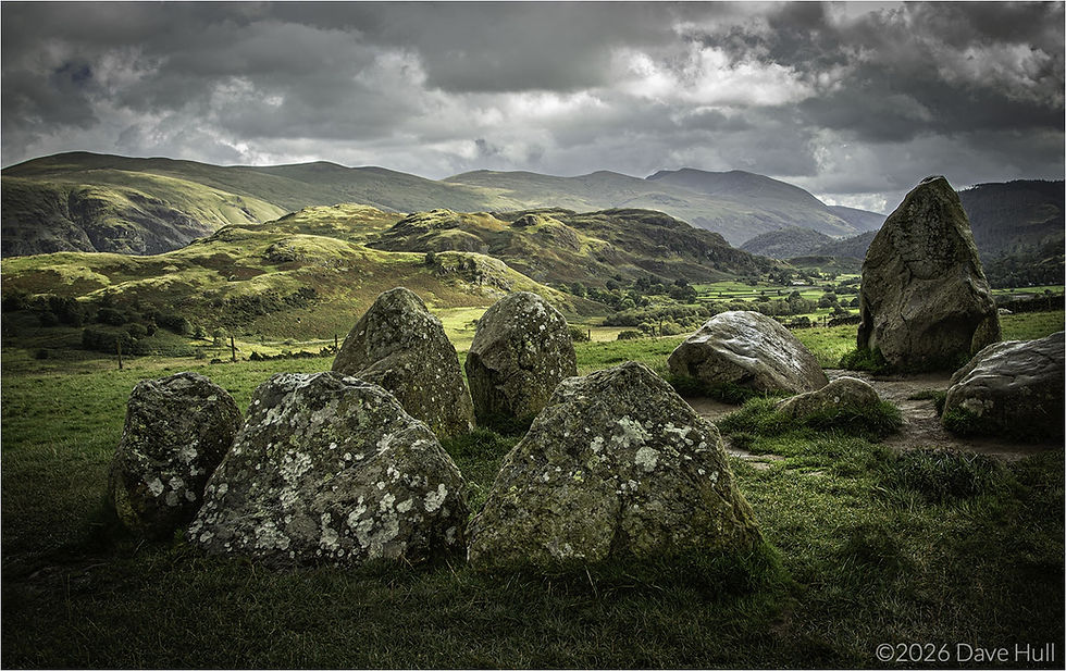 The ancient Castlerigg stone circle in a grassy field, surrounded by green hills under a cloudy sky. Peaceful and moody atmosphere.