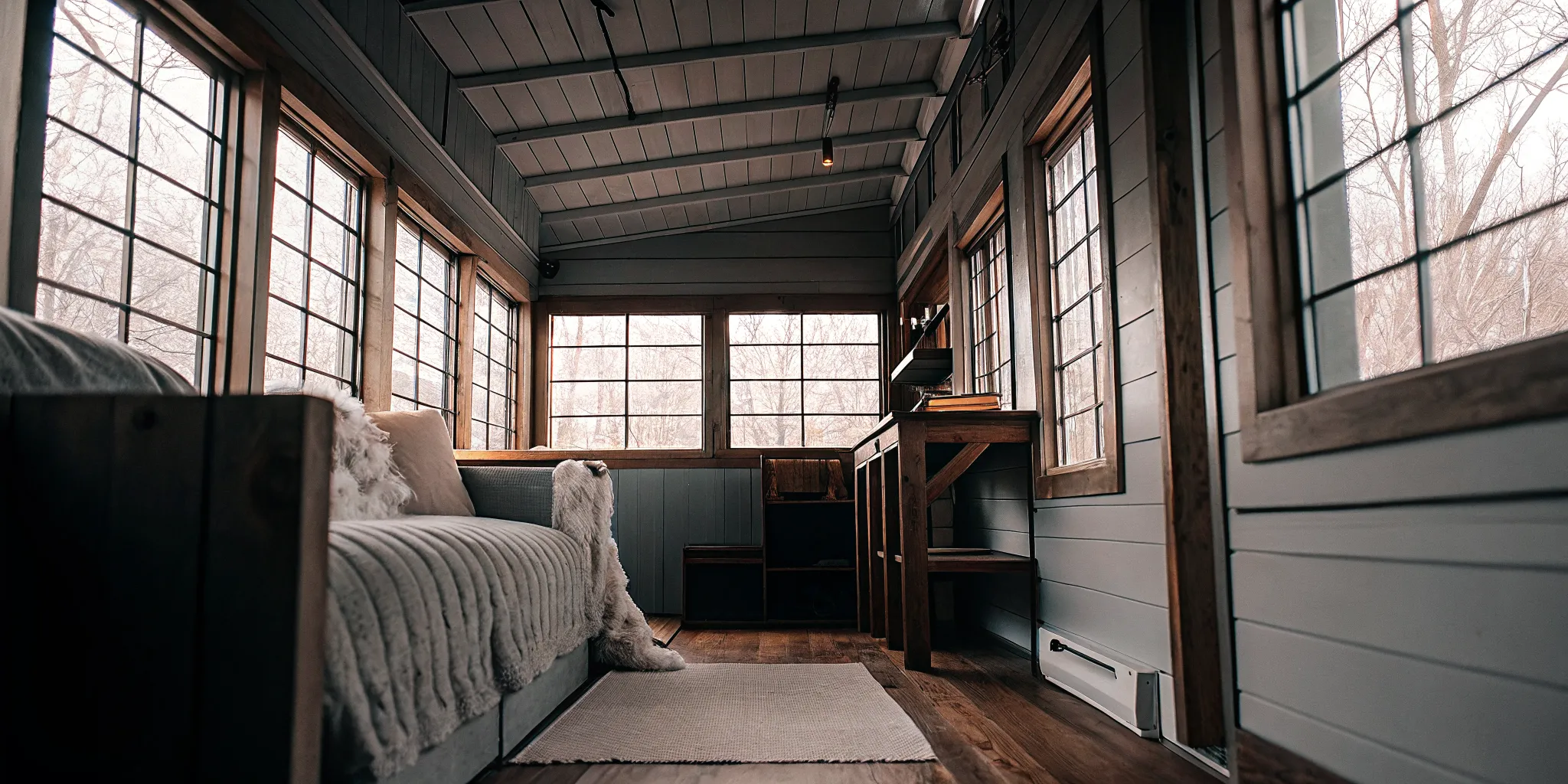 Interior of a converted shipping container tiny home with insulation, wood flooring, and large windows creating a cozy living space