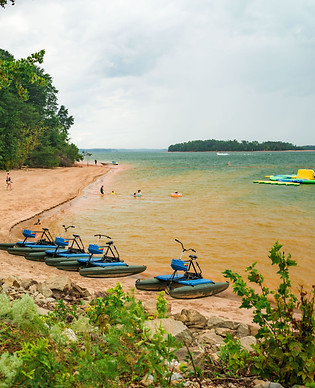 Hydrobikes on the shoreline of Lake Hartwell with people playing and swimming in the background.