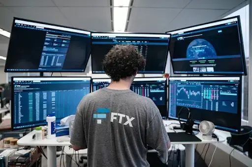 A picture of FTX's Founder Sam Bankman-Fried in front of multiple computer monitors.