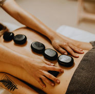 A relaxing spa setting with a client lying face down on a massage table, smooth heated basalt stones placed along their back. Soft lighting, calming ambiance, and a massage therapist gently working to enhance relaxation.