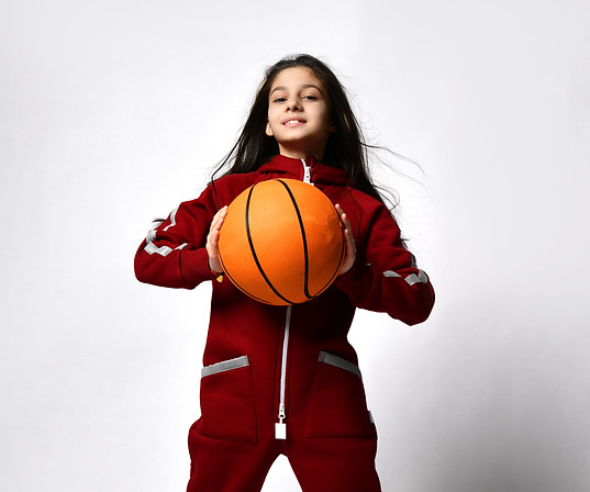 stylish teenage girl in burgundy warm overalls posing at the camera with a basketball. Spo