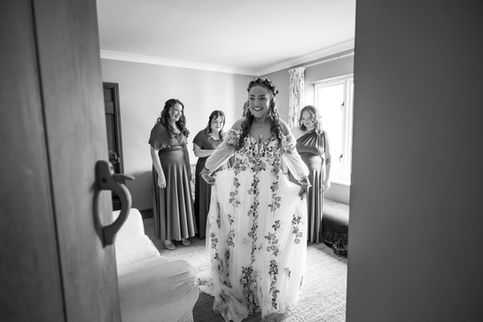 A bride reveals her wedding dress to her bridesmaids at a wedding in Devon. Captured in black and white by Fox and Co Photography.