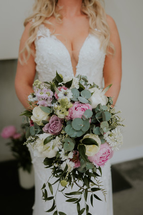 Bride in lace wedding dress holds a romantic pink and white floral bouquet before the ceremony in Cornwall.