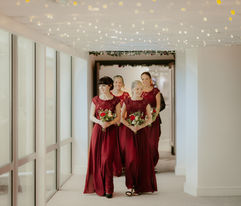 Bridesmaids walk in unison wearing red dresses with soft lighting before a wedding in Cornwall.