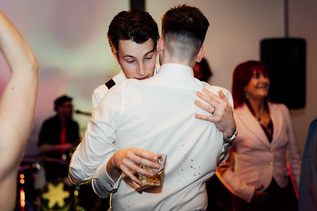 The groom hugs a guest and spills some of his drink 