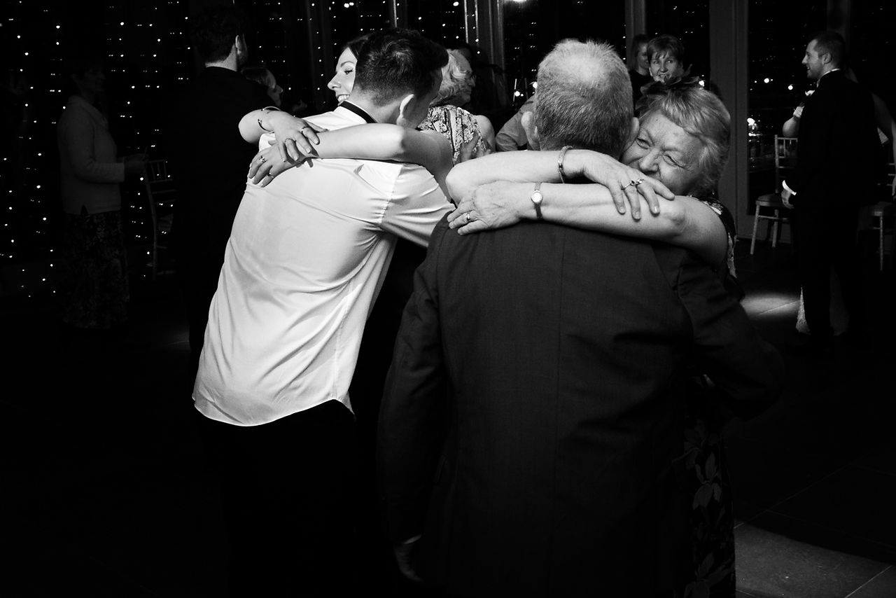 two female guests hug their partners at the same time during a wedding
