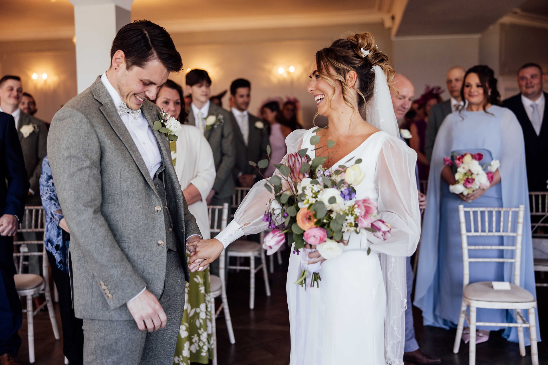 The bride holds the grooms hand as she reaches the front of the aisle at their wedding. 