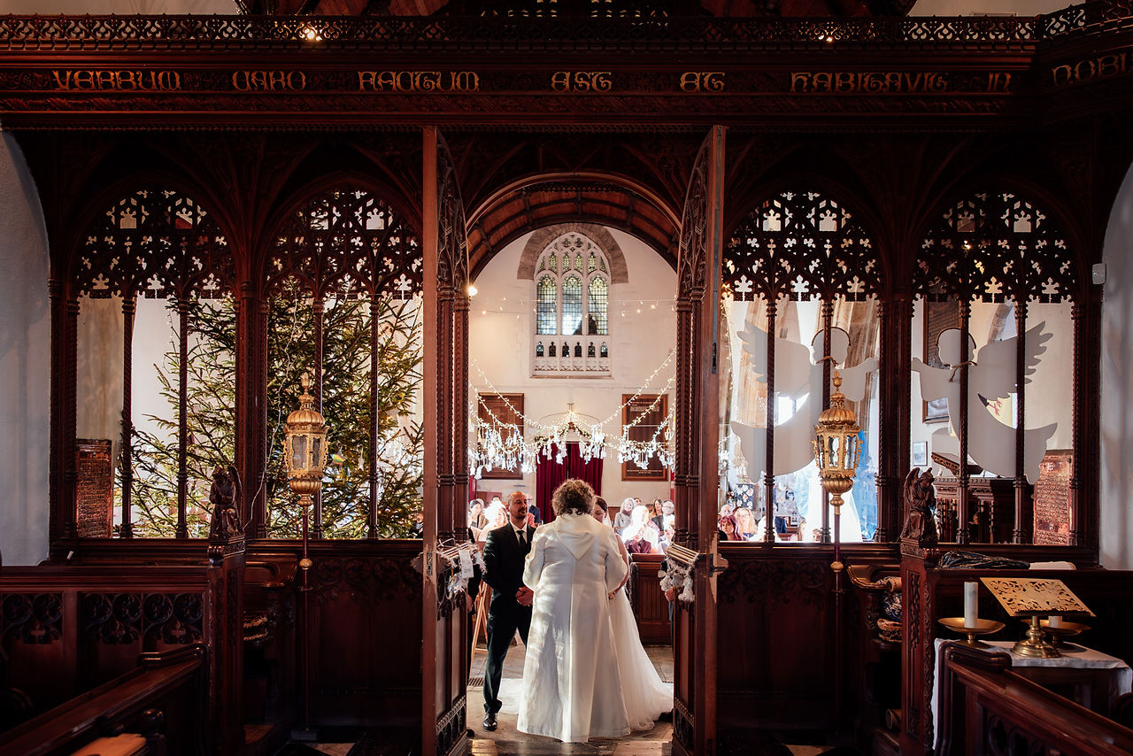 The bride and groom stand beneath a tall arch way during their church wedding ceremony