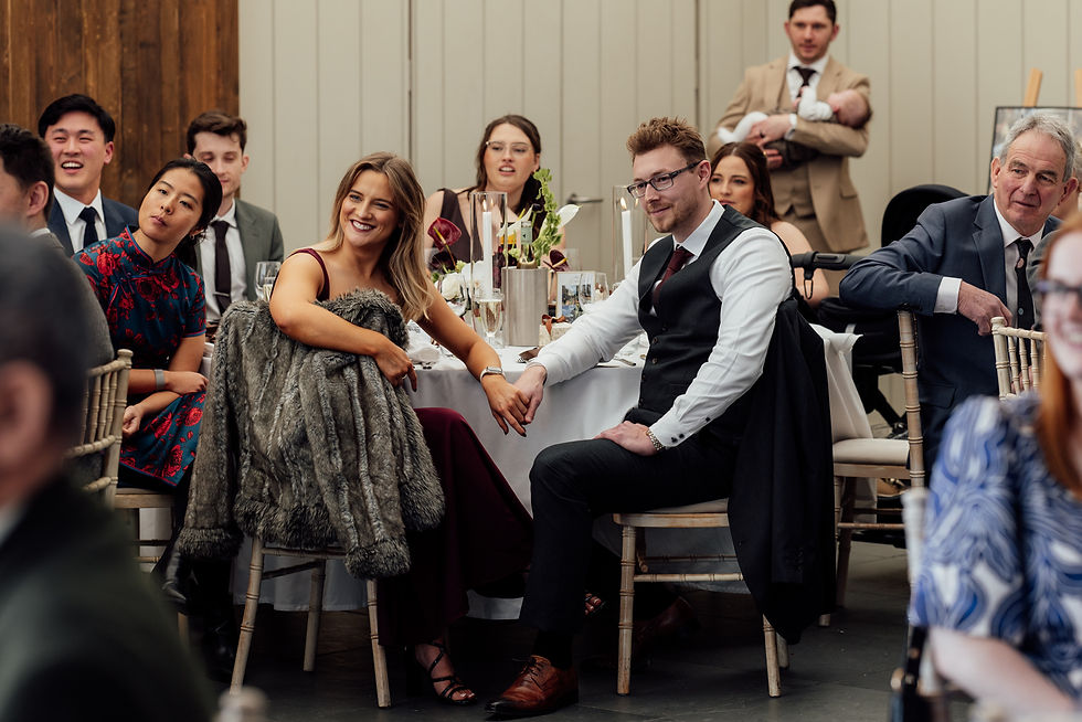 Guests hold hands and laugh during a speech at a wedding in Devon captured by award winning wedding
