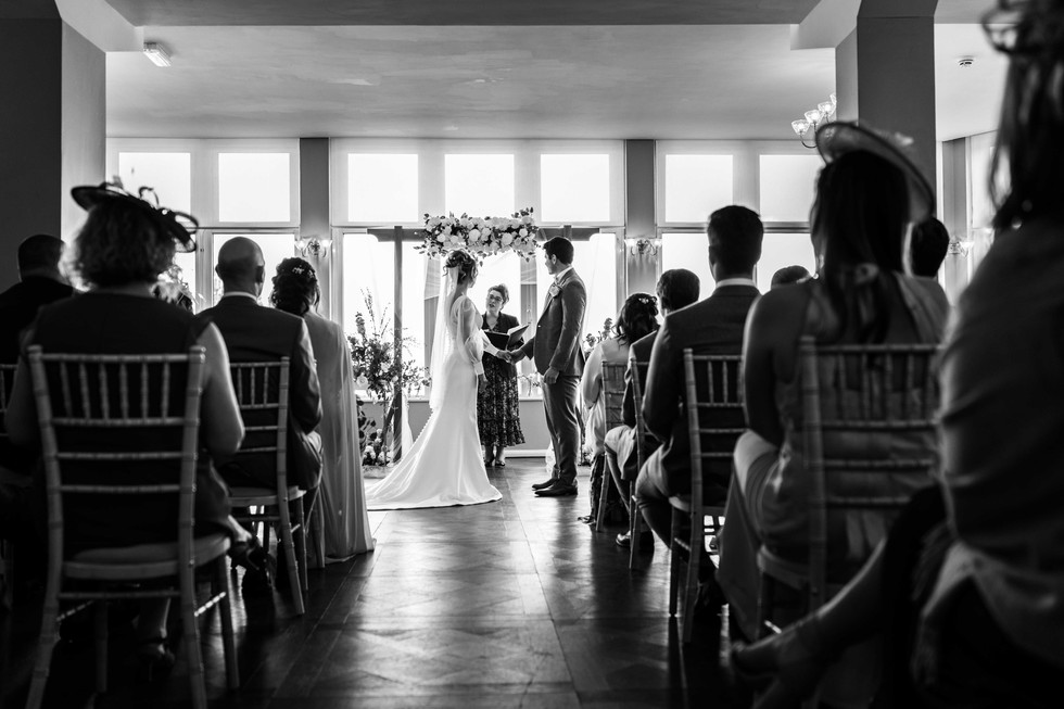 The bride and groom hold hands during a wedding ceremony. Captured in black and white by Fox and Co Photography during a wedding in St Ives. 