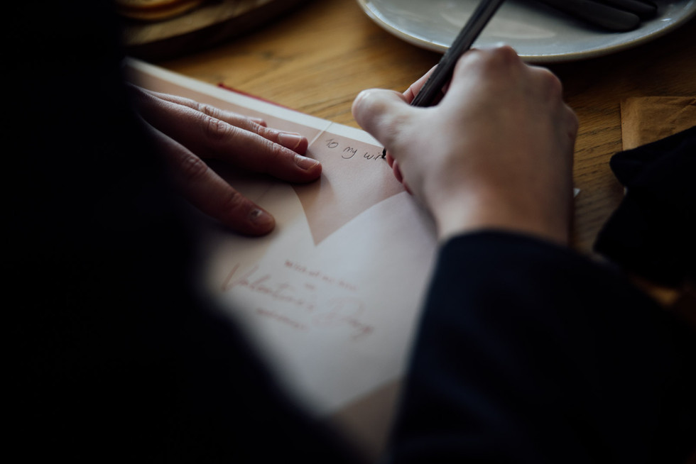A groom writes a valentines card to his wife before their wedding
