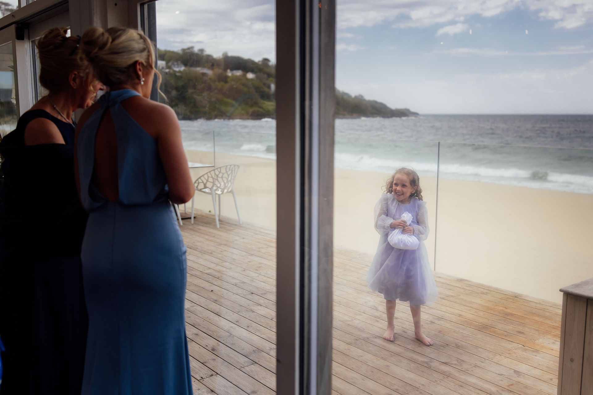 A child smiles at guests whilst stood outside during a wedding at The Carbis Bay Hotel in Cornwall