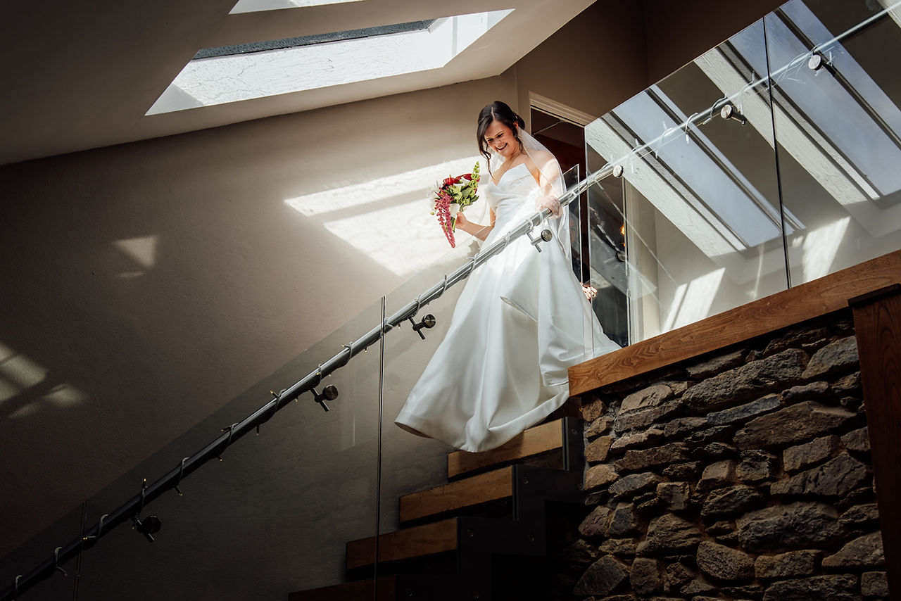 A bride descends the stairs at Trevenna in Cornwall as a ray of light illuminates her and her wedding dress. 