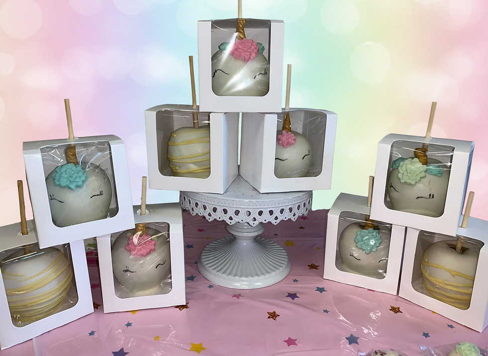 Landscape photo of unicorn-themed candy apples in white boxes arranged on a white cake stand and pink star-patterned tablecloth, landscape aspect ratio.