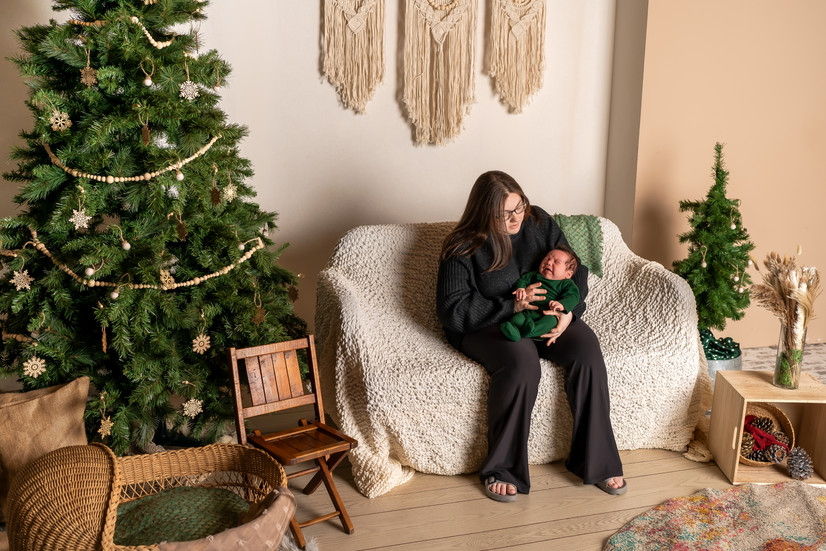 Des Moines, Iowa Family Photograph - neutral boho-inspired holiday set up including couch, tree, and wooden ornaments with mother and newborn baby present