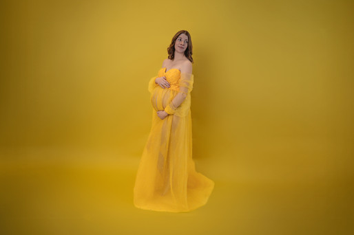 Des Moines, Iowa maternity and newborn photographer - pregnant woman resembles Disney Princess, Belle, in a yellow off the shoulder dress on a yellow backdrop.