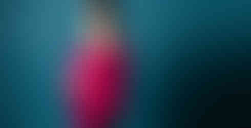 Des Moines and Norwalk, Iowa pregnancy photos - woman with long dark hair in a long hair and bright pink maternity gown with flowy sleeves poses in front of a blue backdrop with her hands on her belly.