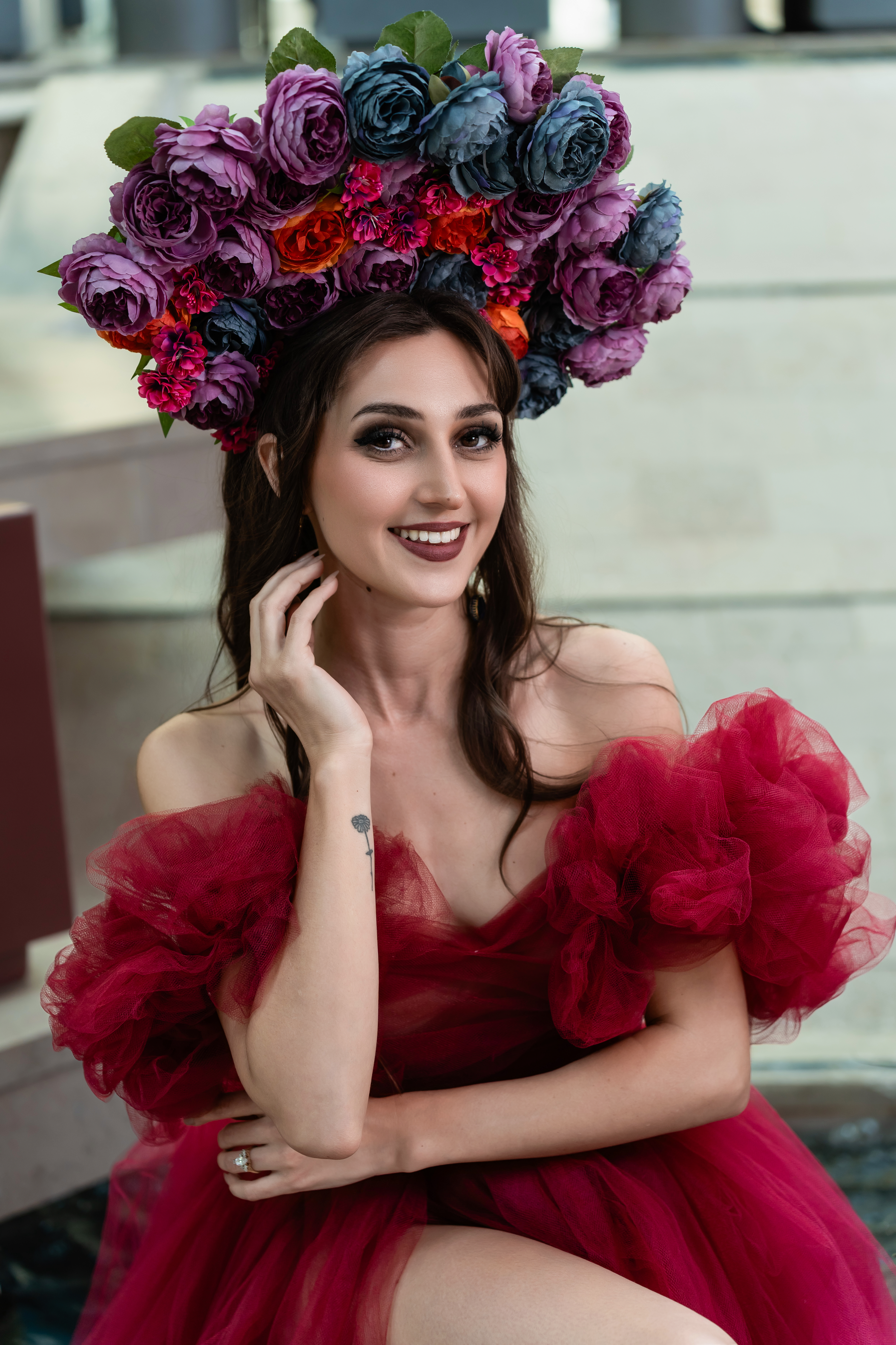 Des Moines, Iowa glamour and boudoir photographer - a woman in a red gown and a large decorative floral head piece smiles at the camera.