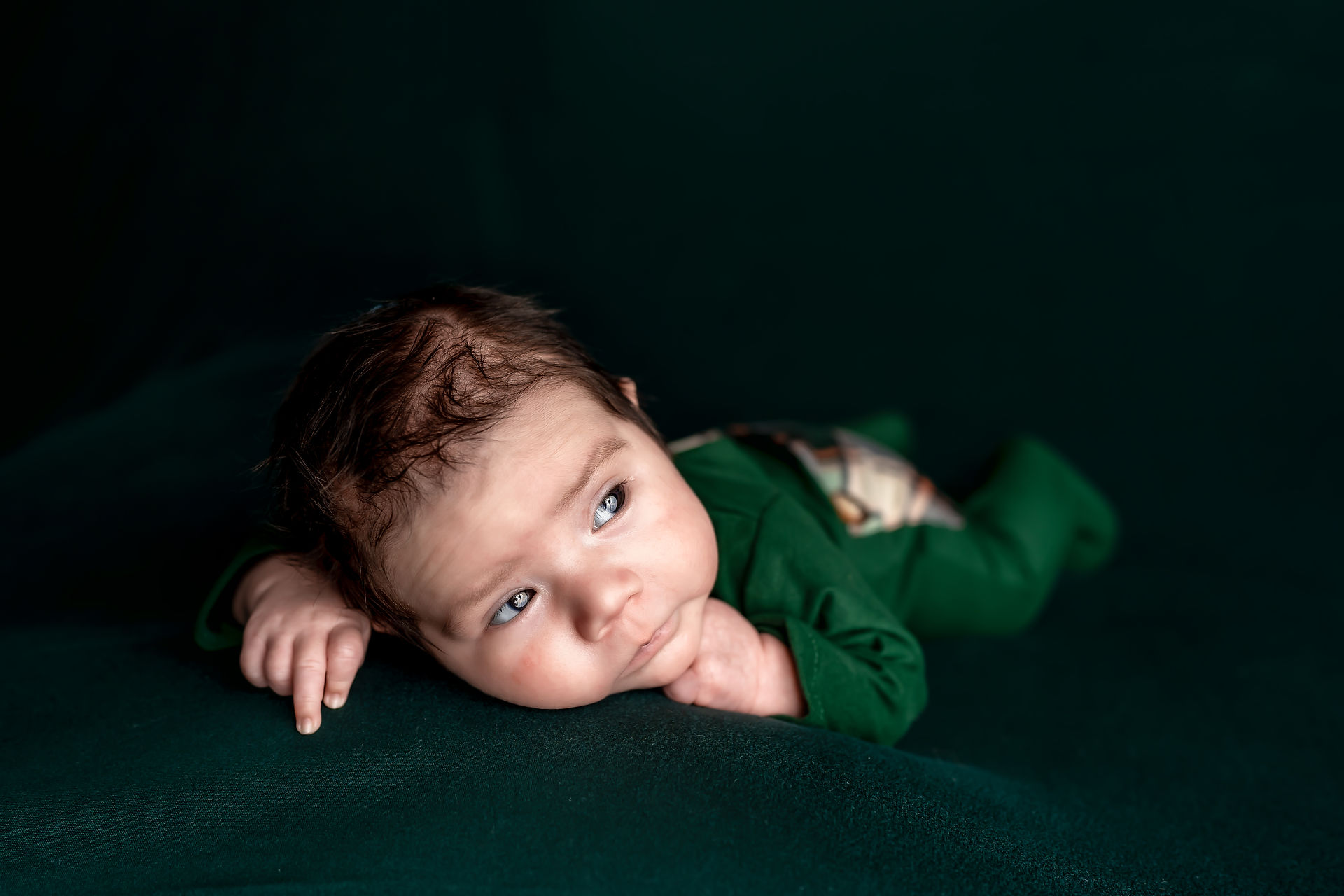 Des Moines, Iowa Newborn Photographer - newborn baby boy lying on tummy in green outfit on green background looking  away