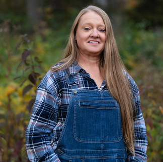 Des Moines, Iowa portrait photographer - woman with long blonde hair is wearing a flannel shirt and overalls, stands with her hands in her pcokets.