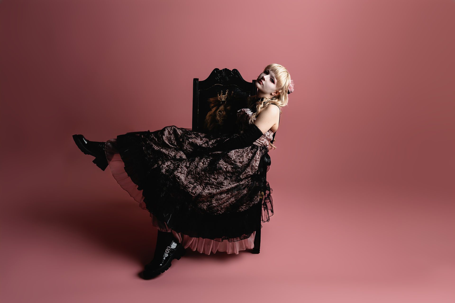 Des Moines, Iowa high school photographer - high school senior wearing a black and pink prom dress and platform shoes leans back in a black chair with one foot up against a pink backdrop.