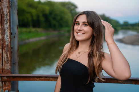 Des Moines, Iowa senior photographer - teenager girl with dark hair pulled into a messy bun is staying on a wooden and metal bridge.