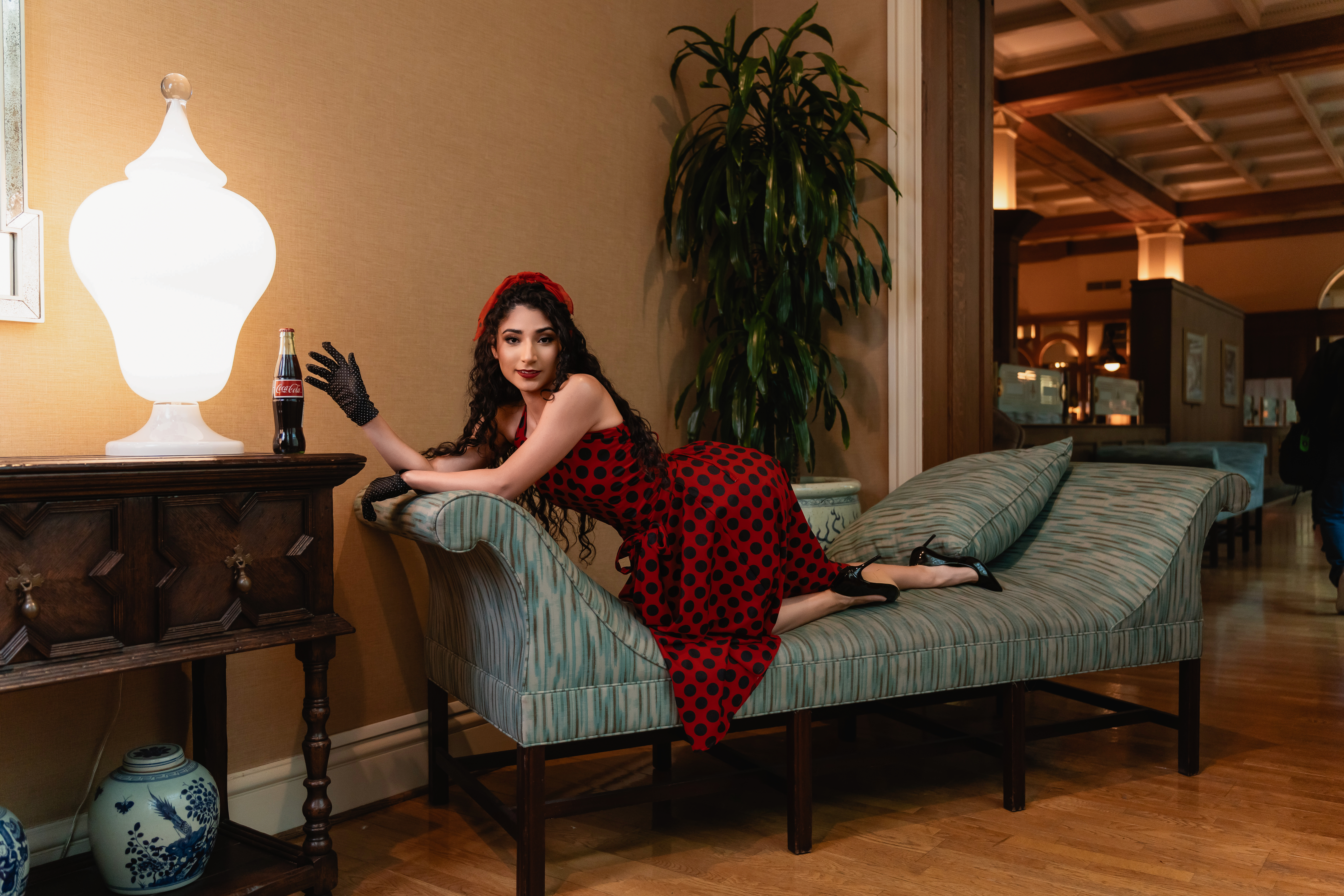 Des Moines, Iowa boudoir and pin-up photographer - woman in a vintage polka dot dress leans on a chaise lounge toward a glass bottle of coca-cola.