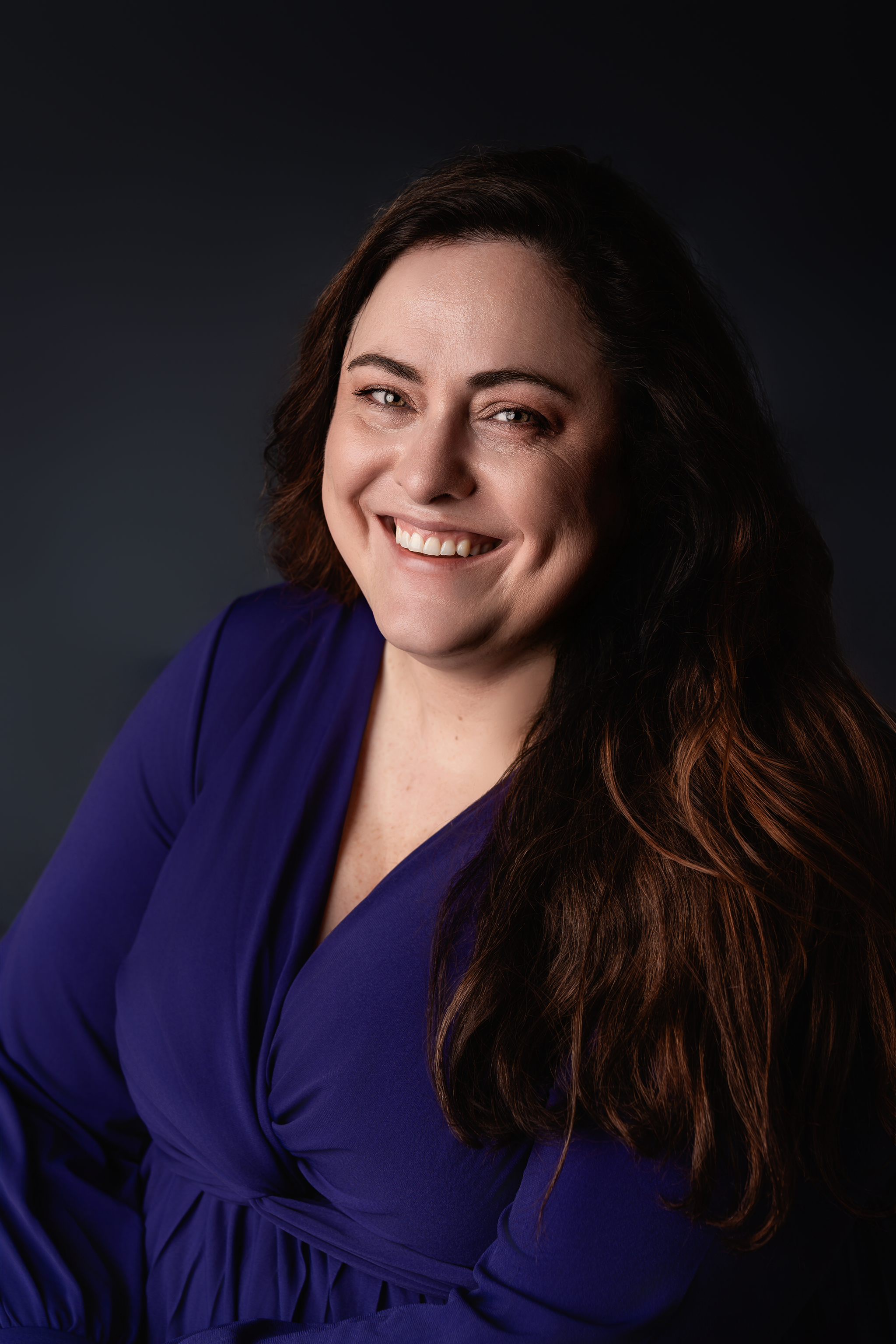 Des Moines, Iowa headshot and branding photographer - woman in a purple blouse and dark hair smiles for her headshot.