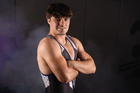 Calli Tuggle Photography - Des Moines, Iowa area senior photographer - a male high school senior wearing his Norwalk wrestling singlet crosses his arms in the wrestling room.