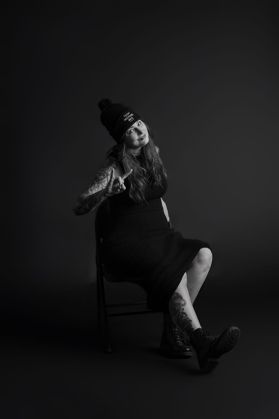 Des Moines and Norwalk, Iowa photography - black and white image of a female dressed in all black dress and stocking hat sitting on a black chair giving the 'rock on' sign.