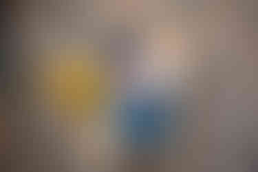 Des Moines and Norwalk, Iowa newborn photographer - a newborn baby boy is swaddled in a blue blanket with his feet out on a rainbow bed with yellow flowers near it.