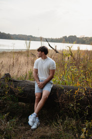 Des Moines, Iowa senior photography - teenage male sits on a large piece of driftwood and looks off into this lake.