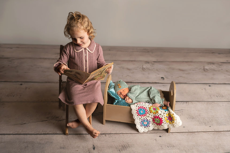 Des Moines Newborn Photographer - infant baby girl lying on tummy on a newborn bed, toddler aged female in a purple dress sitting beside her reading an antique fairytale book.