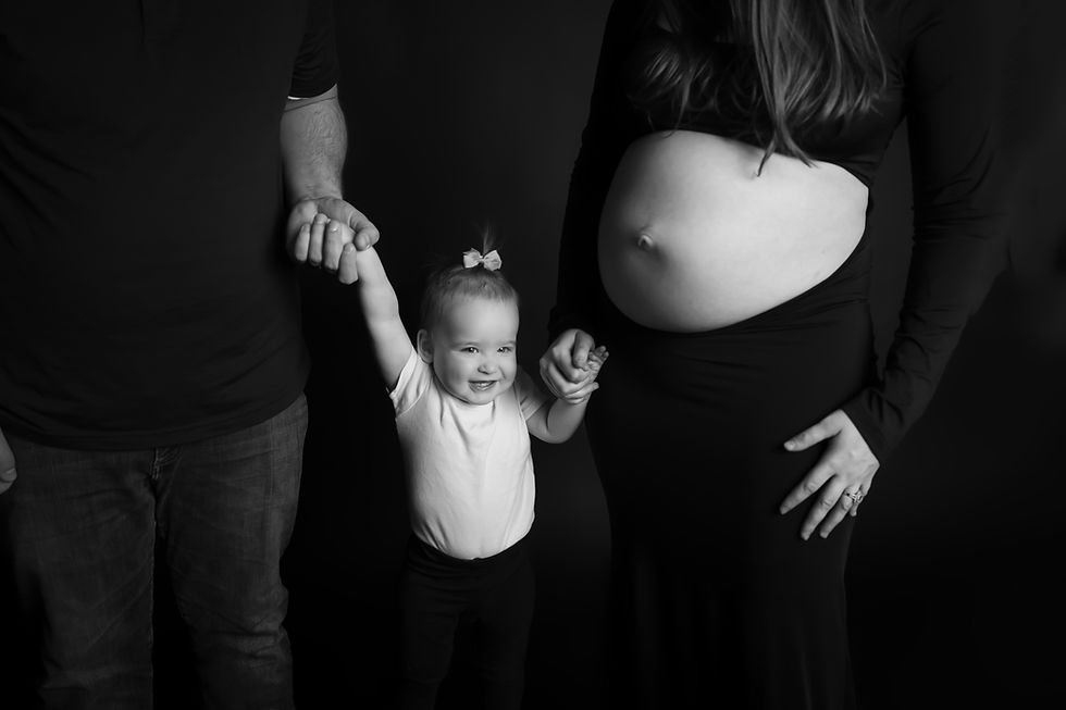 Des Moines, Iowa Pregnancy Photos - black and white image of mom and dad holding a toddler's hands between them. Mom is visibily pregnant with her belly showing.