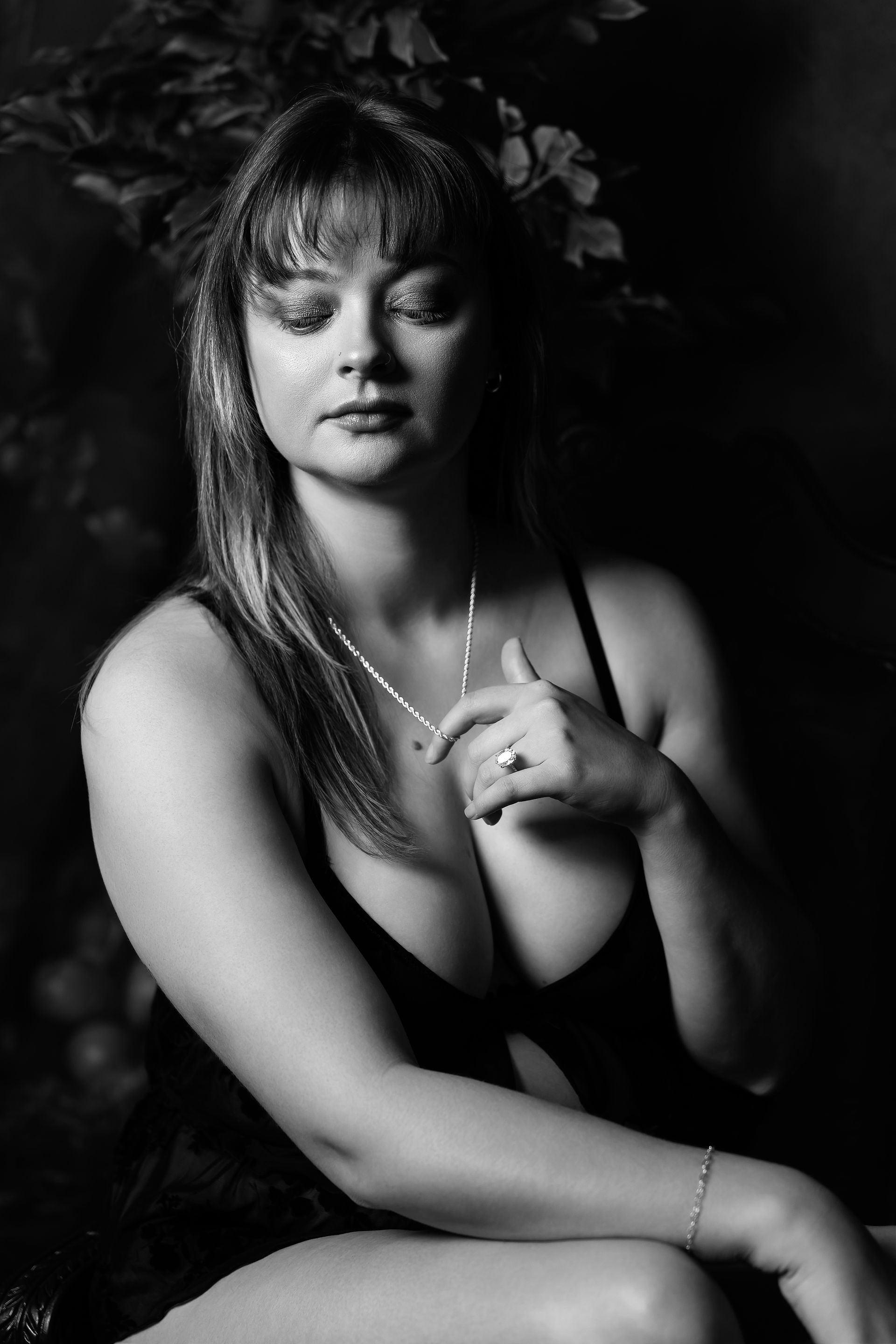 Des Moines, Iowa boudoir and pin-up photography - black and white image of a woman in lingerie adjusting her necklace with her eyes closed.