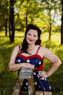 Des Moines, Iowa boudoir and pin-up photography - a woman is wearing a 1940's inspired blue dress with white stars and red trim, leaning against a wooden latter with one hand on her hip. The woman has retro hair and make up.