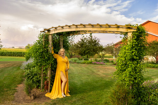 Norwalk, Iowa photographer - Mother-to-Be poses for her maternity session in a yellow gown with a archway behind her.