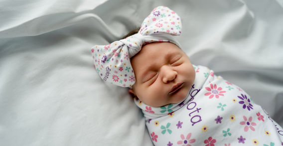 Des Moines, Iowa newborn and Fresh 48 photography - infant girl swaddled in a floral blanket with matching headband against a simple white sheet.