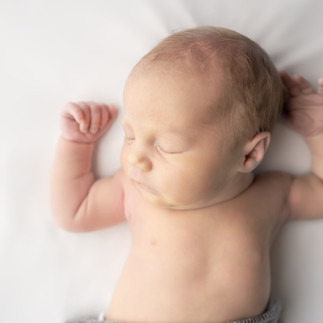 Des Moines, Iowa newborn photographer - newborn baby girl asleep on her back on a white background with her hands above her head.