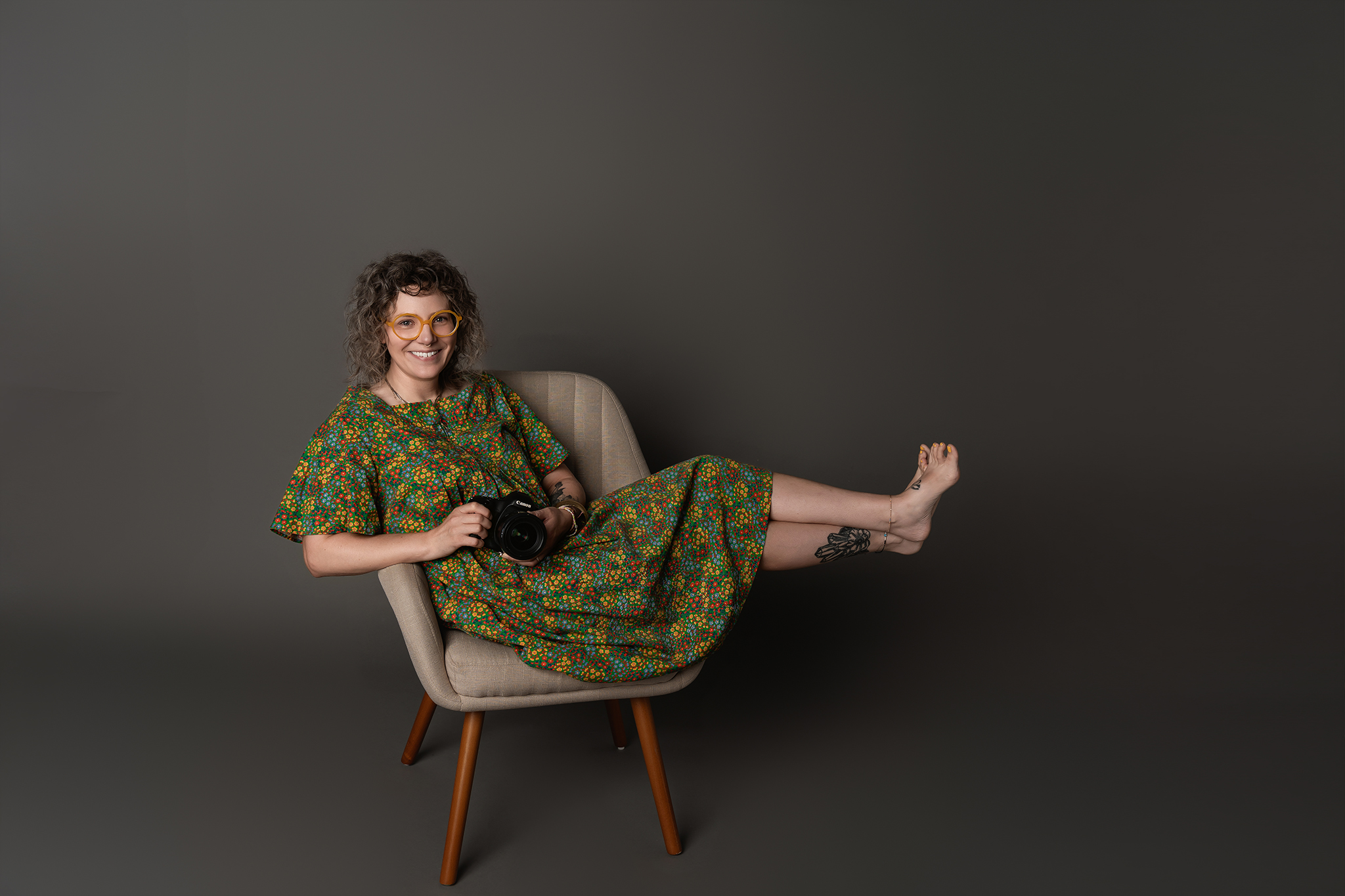 Des Moines, Iowa headshot and branding photographer - woman in a green dress sits in a tan chair holding her camera.