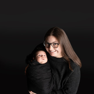 Des Moines, Iowa newborn photographer - New mother holding her infant son swaddled in a black cloth on a black background